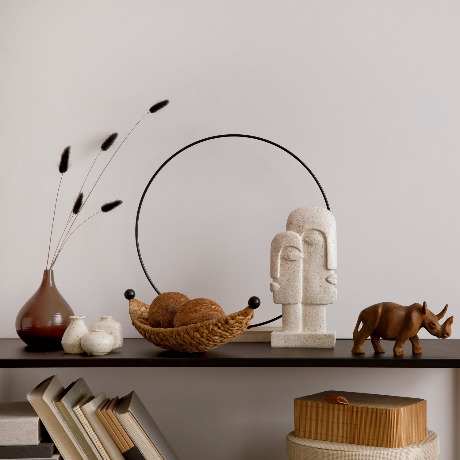 Minimalist shelf arrangement with decorative vases, woven bowl with balls, abstract stone sculpture, and wooden rhino figurine