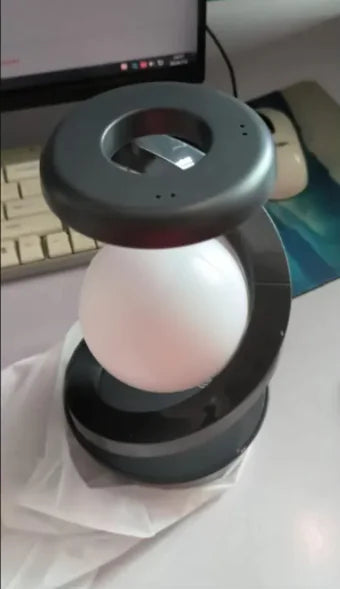 Rotating Moon Desk Lamp with Wireless Charging featuring a suspended orb within a sleek black curved frame for ambient lighting