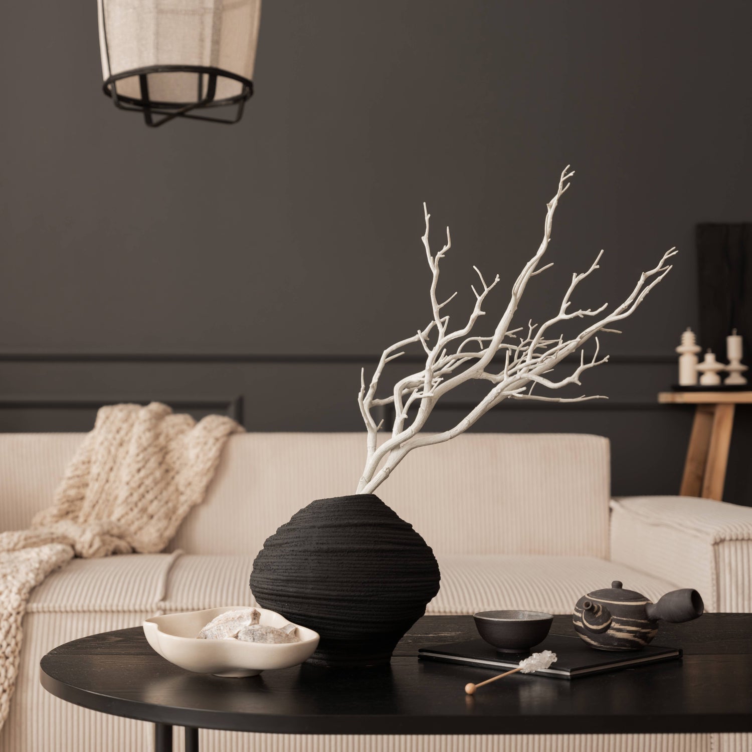Black textured vase with white branches on a round black coffee table in a neutral-toned living room