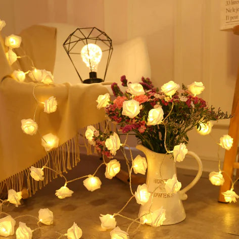 LED Rose Flower String Lights softly glowing with warm white bulbs draped over a cozy chair and floral pitcher arrangement